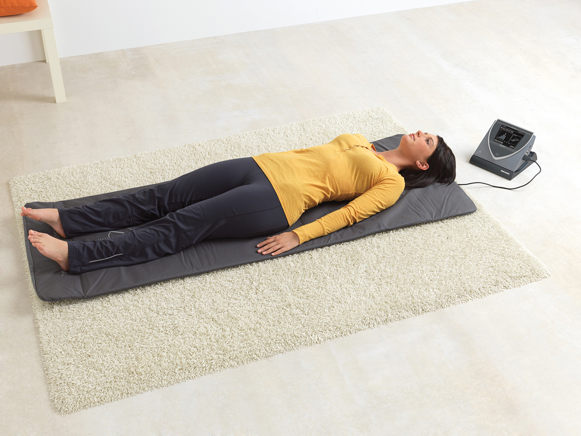 Frau auf Bodenmatte mit Therapiegerät