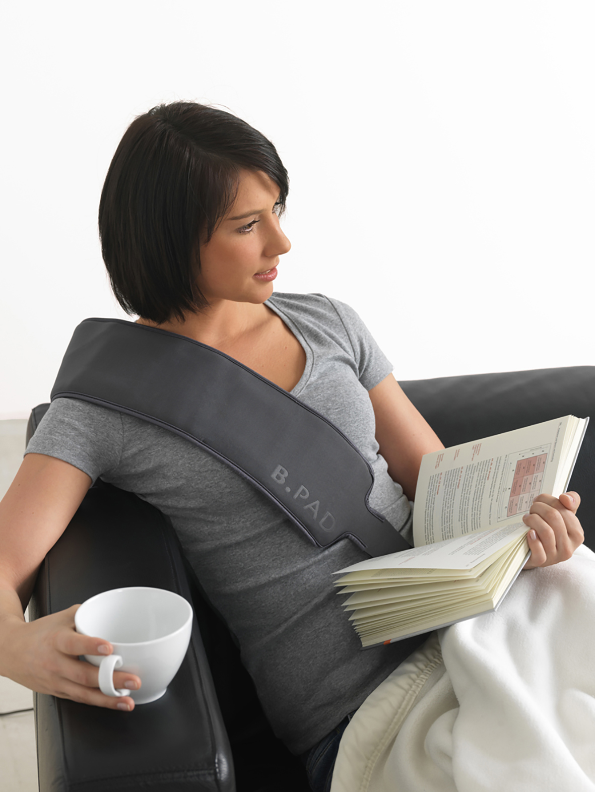 Frau mit Therapiegerät, Kaffeetasse und Buch